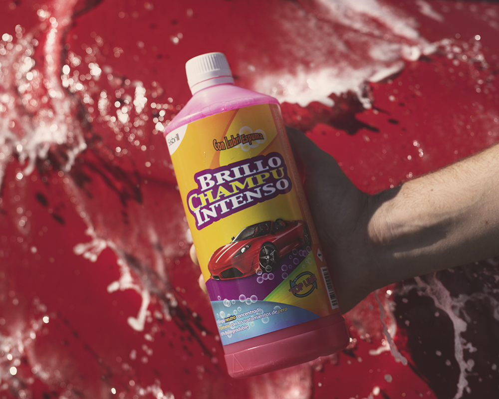 Bouteille de Champú Brillo Intenso avec le capot d’une voiture rouge en arrière-plan