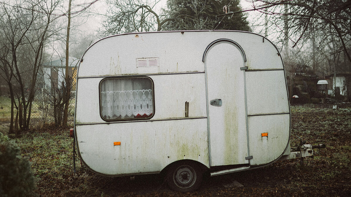 Caravane avec une peinture en mauvais état stationnée dans un jardin arrière