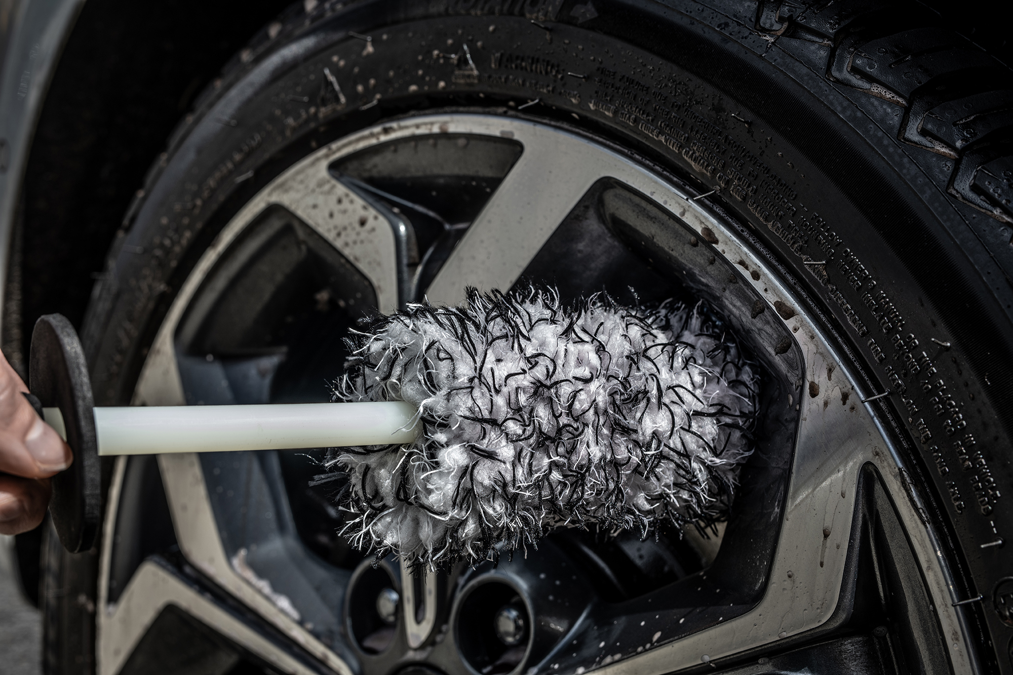 Homme nettoyant une jante noire et le pneu d’une voiture blanche avec une brosse