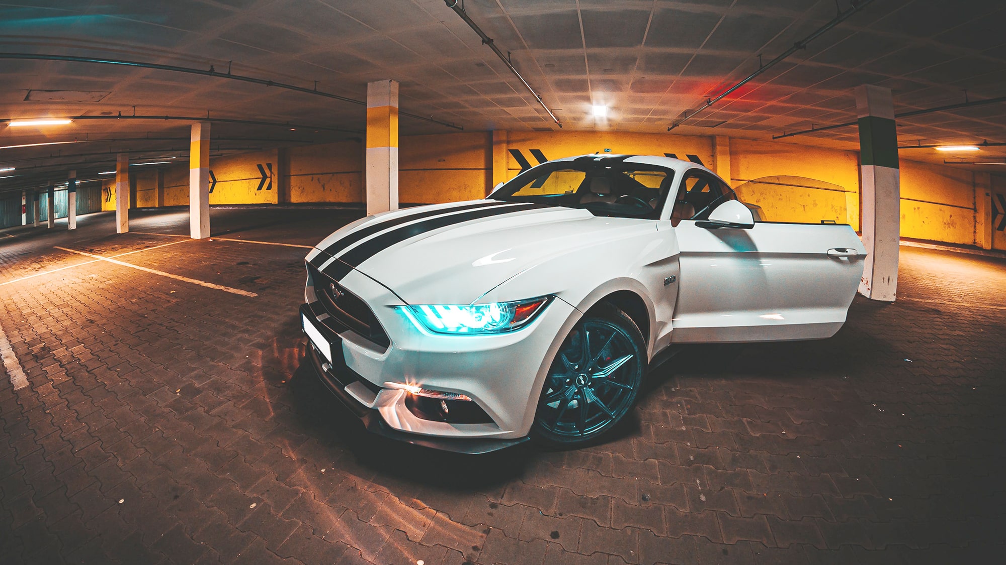 Ford Mustang blanche avec bandes bleues sur le capot dans un parking souterrain