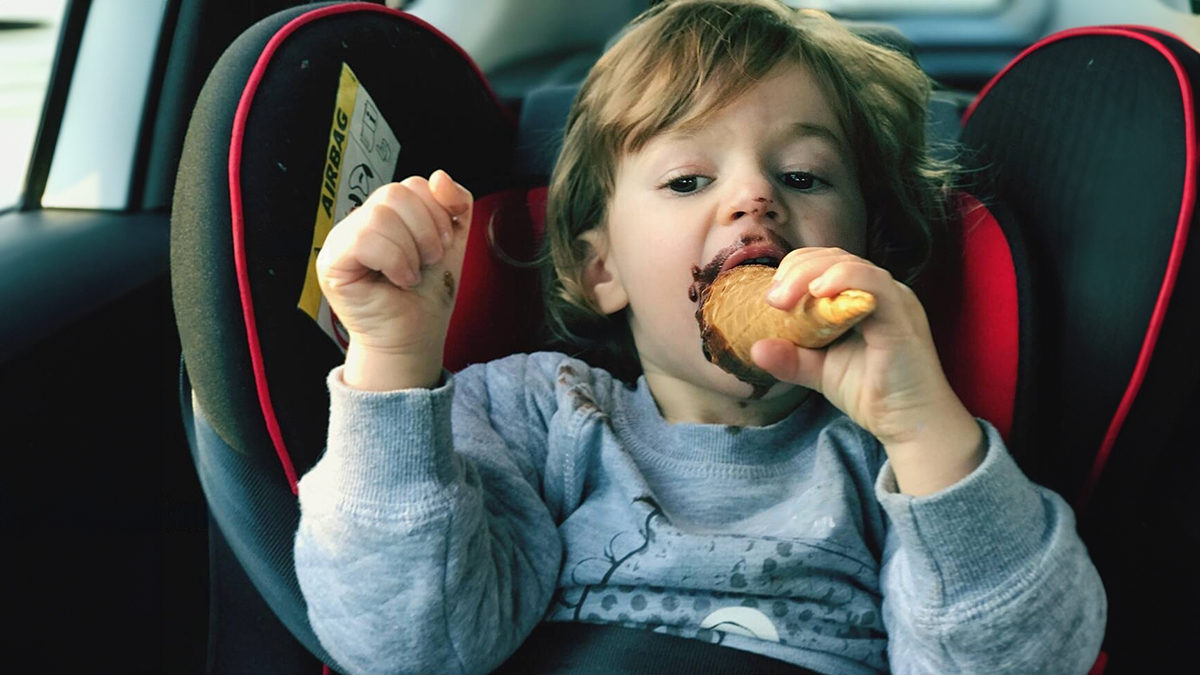 Bébé avec la bouche tachée de chocolat, assis dans son siège auto, en train de manger une friandise