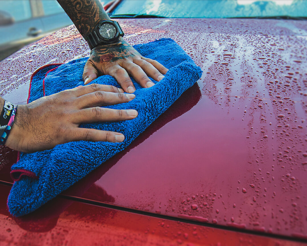 Personne séchant le capot d’une voiture avec une serviette de séchage en microfibre
