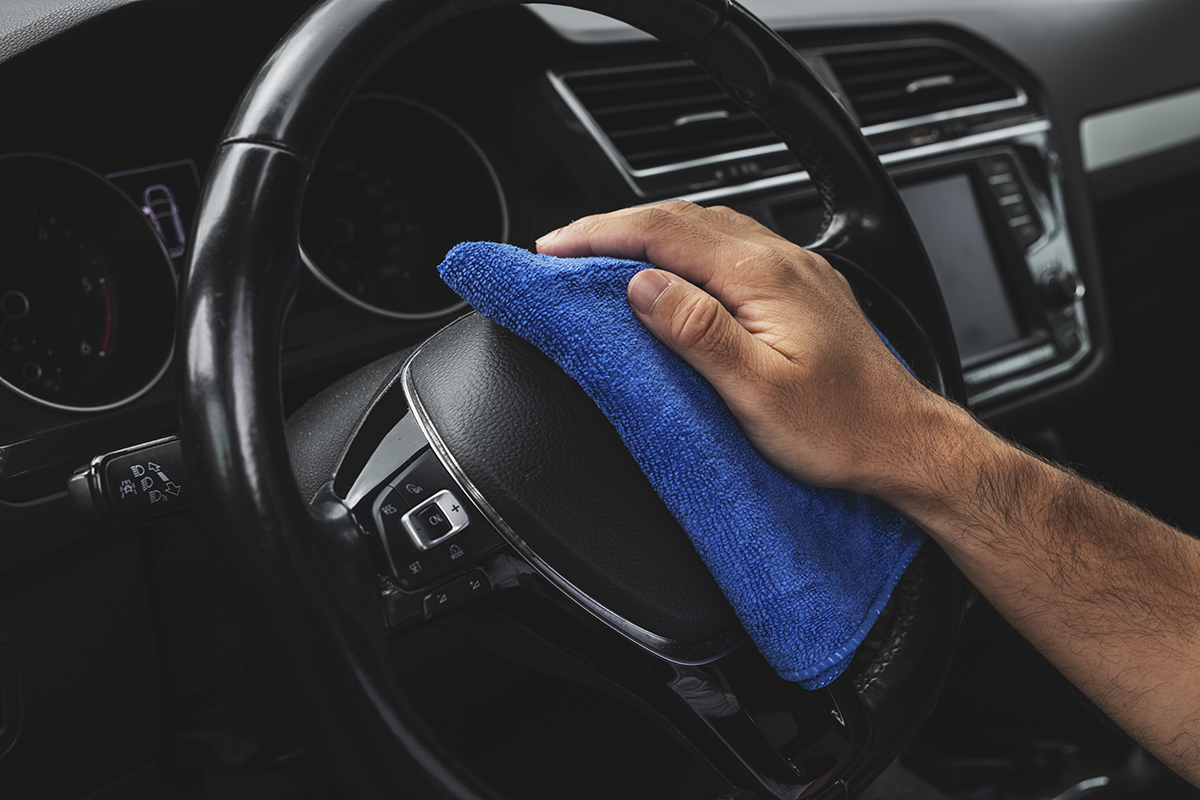 Main d’un homme avec une microfibre posée sur le volant d’une voiture